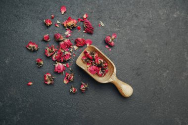 Kurumuş gül tomurcukları ahşap bir kepçeyle kaplanır ve karanlık taş yüzeyine saçılır..