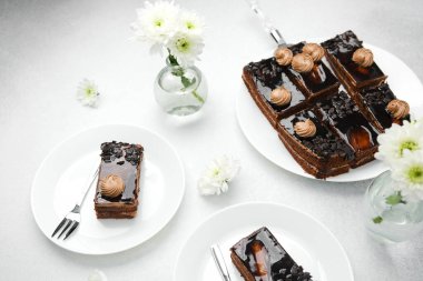 Lezzetli çikolata dilimleri, beyaz tabaklar ve masada krema süslemeleri.