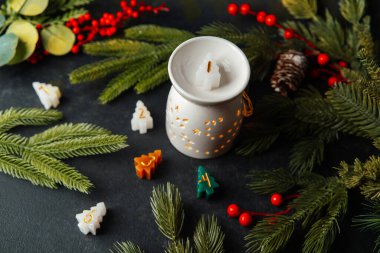 Küçük şenlikli Noel ağacı mumları ve süslemeleri çam dallarıyla karanlık arka planda otururlar.