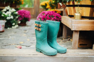 Tokalı bir çift yeşil lastik bot çiçek açan bir verandada duruyor.