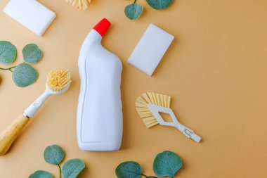 Beyaz temizlik şişesi, fırçalar ve süngerler yeşil arka planda.