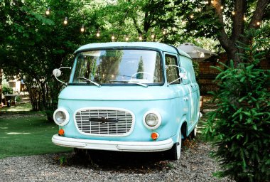 Seyahat ve eski yaşam tarzı stok konsepti için yaz bahçesinde peri ışıkları olan klasik mavi bir minibüs.