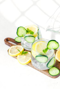 Salatalık limonlu su, tahta tahtada nane, beyaz masada güneş ışığı.