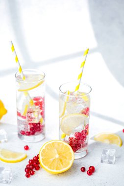 İki uzun bardakta limon kırmızısı üzümlü su ve sarı çizgili kamışlı beyaz masa!