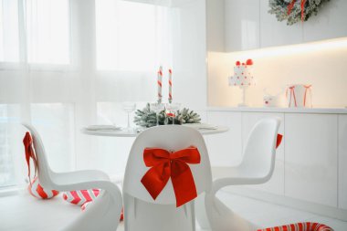 Beyaz modern mutfak masası, şenlikli Noel dekoru ve kırmızı kurdeleli sandalyeler.
