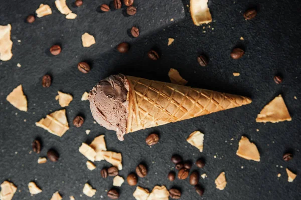 Kahveli dondurma külahı ve siyah arka planda waffle kırıntıları.