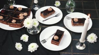 Beyaz çiçekler ve mum ile servis edilen zarif çikolatalı pasta dilimleri.