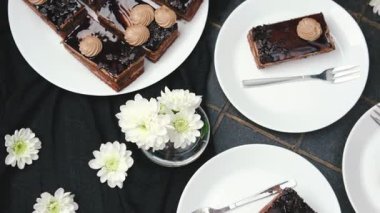 Çatallı ve beyaz çiçekli beyaz tabaklarda servis edilen zarif çikolatalı pasta dilimleri.