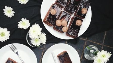 Beyaz çiçekler ve koyu kumaşla süslenmiş beyaz tabaklarda çikolatalı pasta dilimleri..