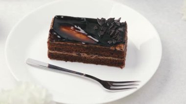 Parlak kremalı zengin çikolatalı pasta dilimi ve çatallı beyaz tabakta siyah pullar.