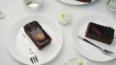 Çatallı ve beyaz çiçekli beyaz tabaklarda servis edilen iki çikolatalı pasta dilimi.