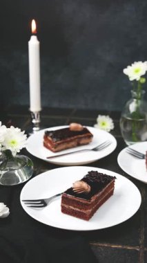 Kremalı çikolatalı pasta ve beyaz tabakta fındık, mum ve beyaz çiçeklerle aydınlatılmış..