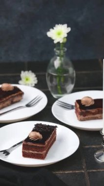 Kremalı üç zengin çikolatalı kek ve çatallı beyaz tabaklarda koyu krema ve mum..