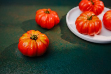 Koyu desenli yüzeyde sıralanmış su damlacıkları olan olgun kırmızı aile yadigarı domatesler.