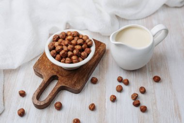 Sürahide fındık sütü, tahtada fındık, beyaz kumaş, kırsal masa ayarı.