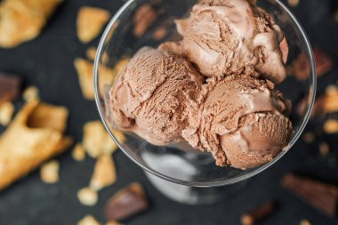 Çikolatalı dondurma kepçeleri karanlık yüzeyde waffle kırıntılarıyla bardakta.