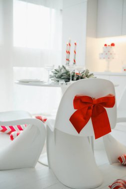 Beyaz sandalyede kırmızı fiyonklu modern yemek masası, tatil dekoru.