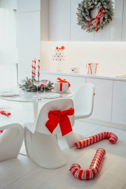 Beyaz modern mutfak masası, şenlikli Noel süslemeleri ve sandalyeli hediyeler.