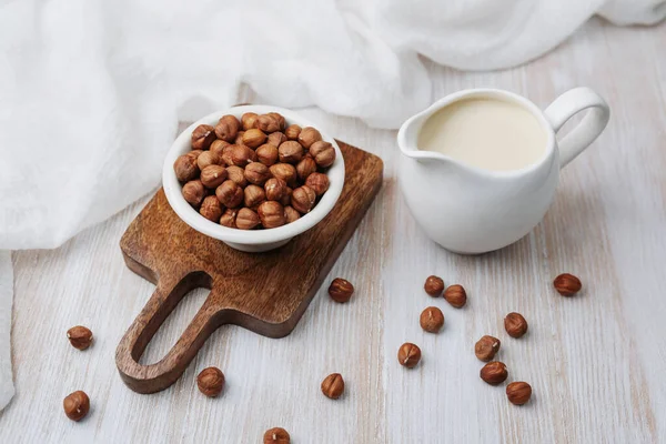 Sürahide fındık sütü, tahtada fındık, beyaz kumaş, kırsal masa ayarı.