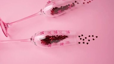 Kırmızı kalplerle dolu zarif kadehler ve Sevgililer Günü için pembe arka plana serpilmiş.