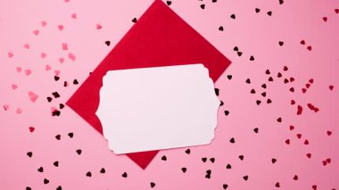 Romantik kırmızı zarf ve pembe yüzeyde Sevgililer Günü için kalp konfetisi olan boş kart.