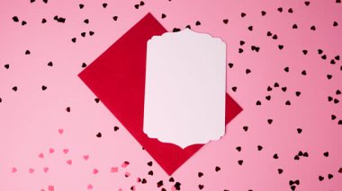 Sevgililer Günü için pembe yüzeyinde dağınık kalp konfetisi olan boş kart ve kırmızı zarf.