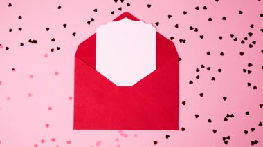 Sevgililer Günü kutlamaları için etrafı kalp konfetileriyle çevrili açık kırmızı bir zarf.