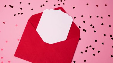 Sevgililer Günü için kalp konfetisiyle çevrili açık kırmızı bir zarf.