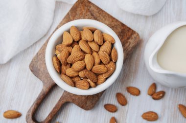 Bademler beyaz kasede. Tahta tahtada sürahi badem sütü ve açık yüzey..