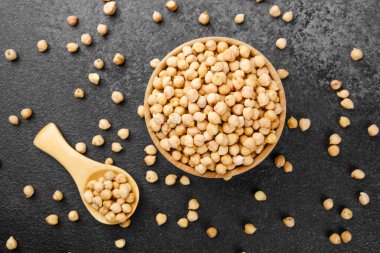 Siyah zemin üzerinde nohut kasesi içinde sebze proteini, sağlıklı beslenme ya da malzeme konsepti için dağınık tanecikler.