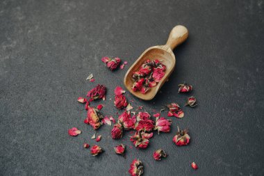 Kurumuş gül goncaları, koyu desenli bir yüzeye saçılmış ahşap bir kepçeyle..