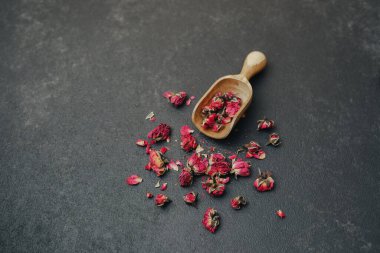 Kurumuş gül tomurcukları, tahtadan kepçenin yanındaki karanlık yüzeye saçılmış.