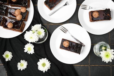 Kremalı ve çatallı siyah çikolatalı kekler beyaz tabaklar, beyaz çiçekler, genel bakış.