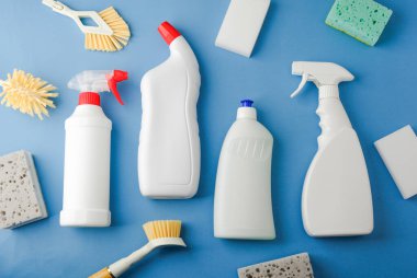 Mavi yüzeye dizilmiş beyaz temizlik şişeleri fırçalar ve süngerler