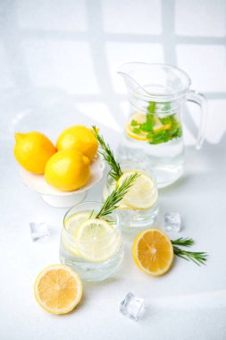 Limon suyunu berrak bardaklarda tazelemek biberiye filizi, buz küpleri ve beyaz arka planda taze limon parçaları.