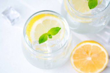 Nane yapraklı limon suyunun yakın görüntüsü buz küpleri ve limon dilimleri berrak arka planda narenciyeli parlak bardaklarda