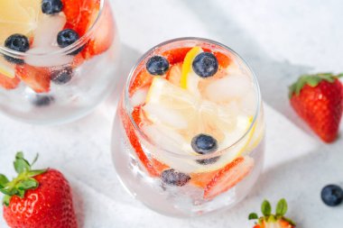 Limonlu, çilekli ve böğürtlenli narenciye içeceğini parlak yaz masasında iki bardakta tazeliyorum.