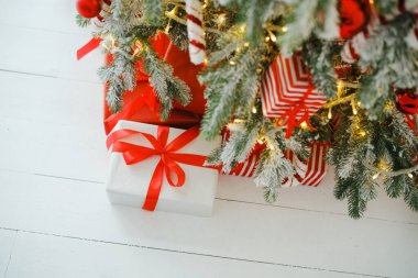 Hediyeler ve ışıklarla süslenmiş, dalların altında bayram hediyeleri, beyaz ahşap zemin.