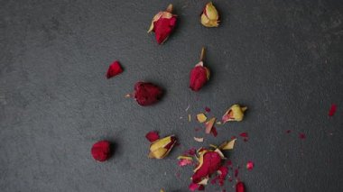 Kurumuş gül tomurcukları gri bir yüzeye saçılmış, bazı yapraklar koparılmış.