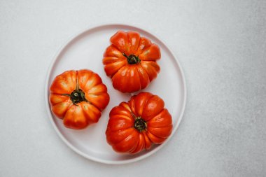 Üç olgun kırmızı domates ve su damlaları beyaz yuvarlak bir tabakta otururlar..