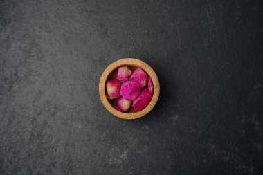 Koyu desenli yüzeyde küçük pembe gül goncaları, üst manzara, doğal malzemeler, çiçek elementleri.