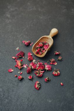 Kurumuş gül tomurcukları küçük bir ahşap kepçeyle koyu dokulu bir yüzeye saçılmış.