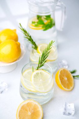 Limon suyunu berrak bardaklarda tazelemek biberiye filizi, buz küpleri ve beyaz arka planda taze limon parçaları.