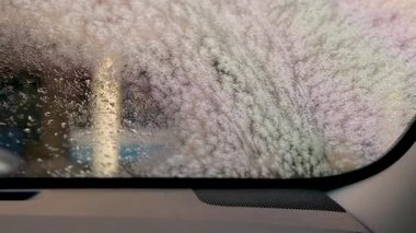Çamaşır yıkarken beyaz sabun köpüğüyle kaplı bir arabanın ön camından görüntüyü al