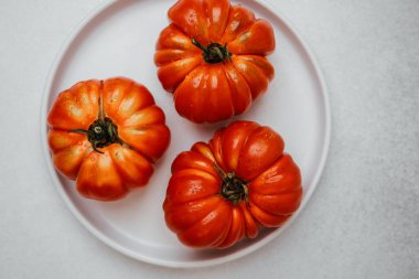 Arkaplanı temiz beyaz bir tabağa su damlalarıyla dolu üç olgun kırmızı domates.