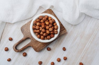 Tahta bir tahtanın üzerinde beyaz bir kasede bütün fındıklar.