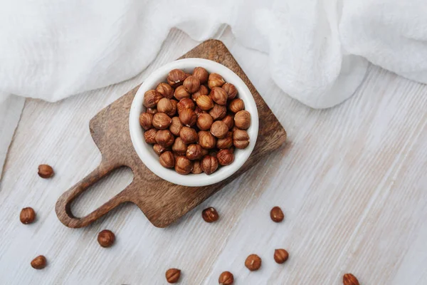 Tahta bir tahtanın üzerinde beyaz bir kasede bütün fındıklar.