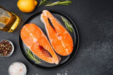 İki somon filetosu siyah bir tabağa konmuş, yanında da limon ve taze otlar var.