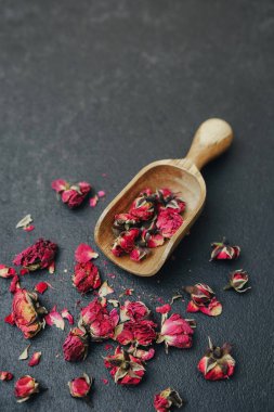 Kurumuş gül tomurcukları, tahtadan kepçeyle karanlık bir yüzeye saçılmış.