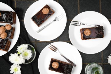 Kremalı ve reçelli üç çikolatalı kek, beyaz tabaklarda, çatallar koyu arka planda, çiçekler...